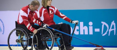 two wheelchair curlers on the rink with a curling stone