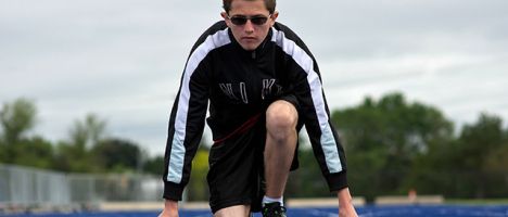 male track athlete in the starting position on a track with trees and cloudy sky