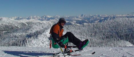 person in a monoski on a mountain summit with mountain range and wide sky in the background